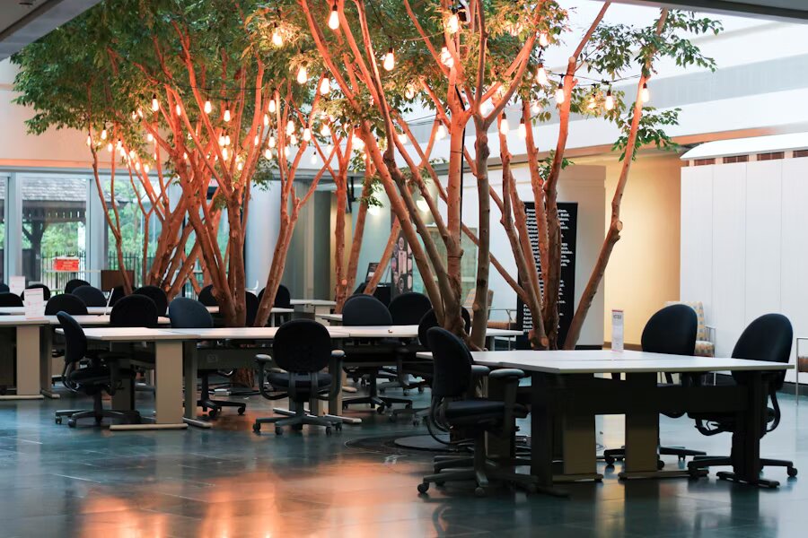 Espace de coworking avec arbres intérieurs, guirlandes lumineuses et grands bureaux partagés